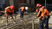 "Four men wearing orange high visibility safety wear tie steel rods together in a frame."